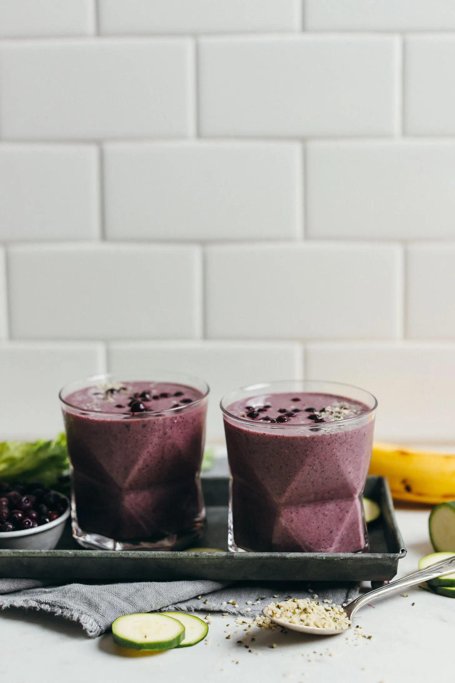 Two glasses filled with our Creamy Zucchini Blueberry recipe and topped with extra blueberries and hemp seeds