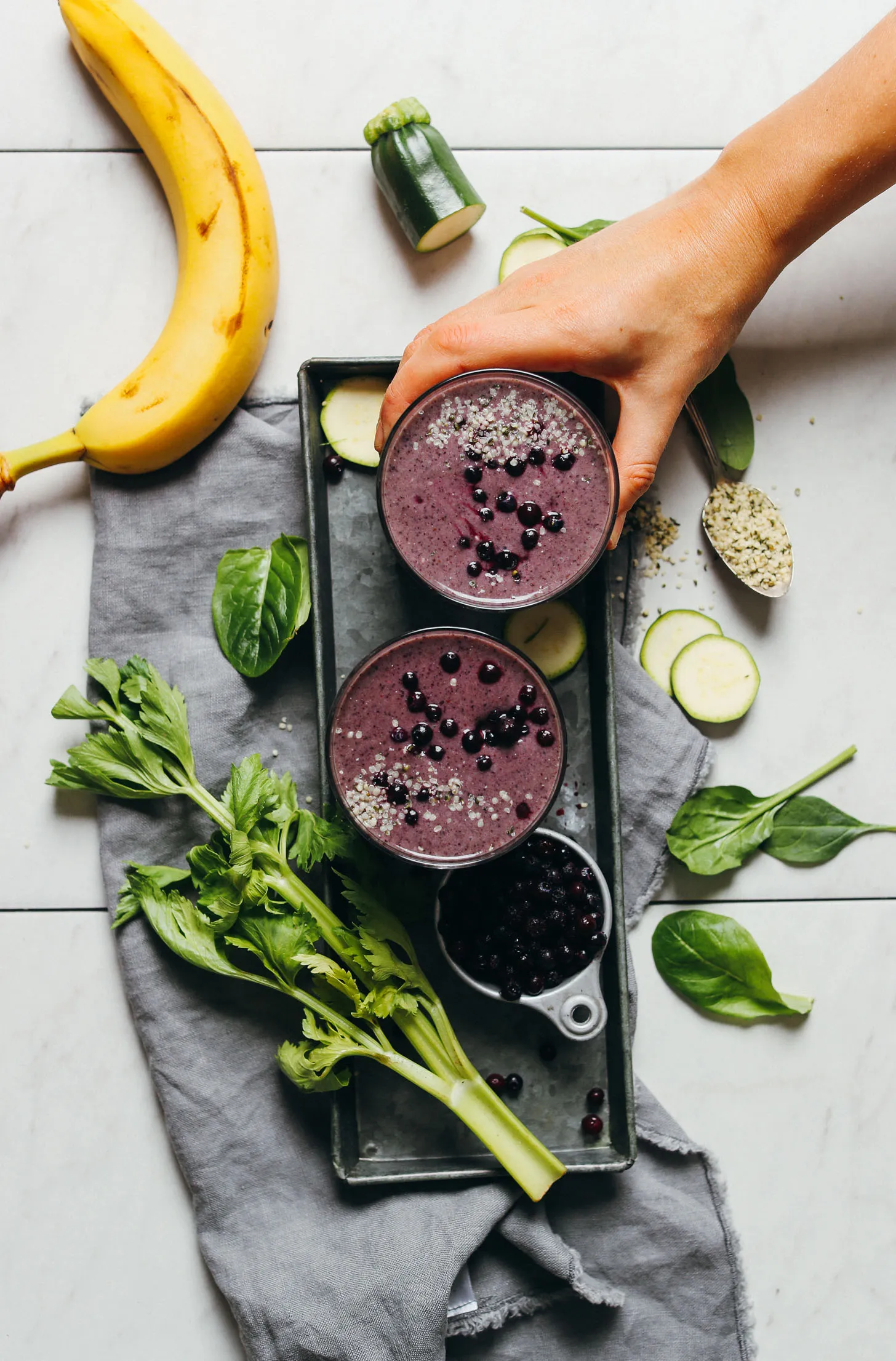 Two glasses of our creamy Zucchini Berry Smoothie with ingredients scattered around